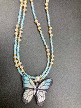Load image into Gallery viewer, This precious sterling silver pendant features a hand-crafted butterfly whose wings have been artistically molded from a basil leaf and painted in a trio of light blue, silver, and gold hues. Accompanying the butterfly pendant are two glass beaded necklaces in an alluring combination of light blue, gold, and medium-small clear glass beads. A stunning summer accessory.  Measurements:  Necklace is 16” adjustable up to 18" in length