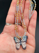 Load image into Gallery viewer, This precious sterling silver pendant features a hand-crafted butterfly whose wings have been artistically molded from a basil leaf and painted in a trio of light blue, silver, and gold hues. Accompanying the butterfly pendant are two glass beaded necklaces in an alluring combination of light blue, gold, and medium-small clear glass beads. A stunning summer accessory.  Measurements:  Necklace is 16” adjustable up to 18" in length
