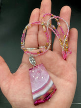 Load image into Gallery viewer, This large agate pendant features a variety of pink hues, from light to dark, and is accompanied by two strands of glass beaded necklaces with pink, silver, gold, and clear beads. The combination of colors creates a stunning and vibrant look, perfect for accessorizing any summer look. Measurements: Necklace is 15” adjustable up to 18" in length