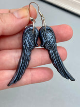 Load image into Gallery viewer, Shimmery silver color angel wings earrings made of polymer clay. These earrings are designed to face forward when worn instead of the front wings showing on the side.