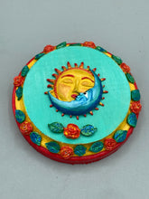 Load image into Gallery viewer, Handcrafted polymer clay wall art with a wood frame, featuring a sun and moon motif complemented with contrasting cool and warm colors. The background is a bright turquoise hue, with marigold flowers and leaves adorning the frame.