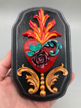 Load image into Gallery viewer, This Sacred Heart Wall Art Decor is the perfect way to enhance your home with an artistic flair. This beautiful artwork features a black wooden frame with a hand-crafted bright red heart. The heart is detailed with dark rose and vibrant green leaves, with a vibrant fire embellishment over the center. Gold decorative embellishments at the sides of the heart add a luxurious touch. H 5 3/8" x W 3 3/8” x D 1 1/2"