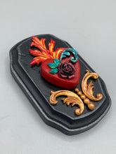 Load image into Gallery viewer, This Sacred Heart Wall Art Decor is the perfect way to enhance your home with an artistic flair. This beautiful artwork features a black wooden frame with a hand-crafted bright red heart. The heart is detailed with dark rose and vibrant green leaves, with a vibrant fire embellishment over the center. Gold decorative embellishments at the sides of the heart add a luxurious touch. H 5 3/8" x W 3 3/8” x D 1 1/2"