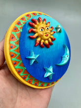 Load image into Gallery viewer, This handcrafted polymer clay wall art on a circle-shaped wood frame with a sun and crescent moon motifs on opposite side and stars. Its cool sky hues, including bright turquoise and dark royal blue, are further complemented by the bright orange and yellow frame adds an extra layer of sophistication to the warm-toned artwork. One of a kind art pieces come ready to hang with a sawtooth hangers in the back. Measurement 4" diameter.