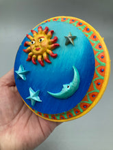 Load image into Gallery viewer, This handcrafted polymer clay wall art on a circle-shaped wood frame with a sun and crescent moon motifs on opposite side and stars. Its cool sky hues, including bright turquoise and dark royal blue, are further complemented by the bright orange and yellow frame adds an extra layer of sophistication to the warm-toned artwork. One of a kind art pieces come ready to hang with a sawtooth hangers in the back. Measurement 4" diameter.