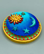 Load image into Gallery viewer, This handcrafted polymer clay wall art on a circle-shaped wood frame with a sun and crescent moon motifs on opposite side and stars. Its cool sky hues, including bright turquoise and dark royal blue, are further complemented by the bright orange and yellow frame adds an extra layer of sophistication to the warm-toned artwork. One of a kind art pieces come ready to hang with a sawtooth hangers in the back. Measurement 4" diameter.