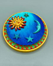 Load image into Gallery viewer, This handcrafted polymer clay wall art on a circle-shaped wood frame with a sun and crescent moon motifs on opposite side and stars. Its cool sky hues, including bright turquoise and dark royal blue, are further complemented by the bright orange and yellow frame adds an extra layer of sophistication to the warm-toned artwork. One of a kind art pieces come ready to hang with a sawtooth hangers in the back. Measurement 4" diameter.