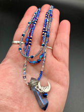 Load image into Gallery viewer, This jewelry piece is a delicate harmony of light and dark tones. Three strands feature a mix of navy blue, pewter, and oval-shaped, light blue-gray beads with a subtle iridescence of amethyst, emerald, and gold. Its celestial theme and bold composition create an alluringly elegant accessory. This whimsical necklace boasts a wonderfully unique aesthetic, featuring a wired blue luster nugget and a whimsical crescent moon charm. Measurements: Necklace is 15 1/4”adjustable up to 18"