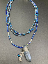 Load image into Gallery viewer, This jewelry piece is a delicate harmony of light and dark tones. Three strands feature a mix of navy blue, pewter, and oval-shaped, light blue-gray beads with a subtle iridescence of amethyst, emerald, and gold. Its celestial theme and bold composition create an alluringly elegant accessory. This whimsical necklace boasts a wonderfully unique aesthetic, featuring a wired blue luster nugget and a whimsical crescent moon charm. Measurements: Necklace is 15 1/4”adjustable up to 18"