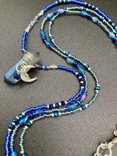 Load image into Gallery viewer, This jewelry piece is a delicate harmony of light and dark tones. Three strands feature a mix of navy blue, pewter, and oval-shaped, light blue-gray beads with a subtle iridescence of amethyst, emerald, and gold. Its celestial theme and bold composition create an alluringly elegant accessory. This whimsical necklace boasts a wonderfully unique aesthetic, featuring a wired blue luster nugget and a whimsical crescent moon charm. Measurements: Necklace is 15 1/4”adjustable up to 18"
