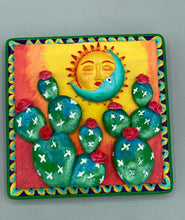 Load image into Gallery viewer, This handcrafted polymer clay wall art boasts a square-shaped wood frame with a sun and crescent moon motifs. Its warm sky hues, including yellow, orange and dark red, are further complemented by hand sculpted cacti plants with cool green-blue tones and dark pink flowers. The dark green frame adds an extra layer of sophistication to the warm-toned artwork. One of a kind art pieces come ready to hang with a sawtooth hangers in the back. H 5" x W 5” x D 1 1/2"H 5" x W 5” x D 1 1/2"