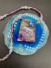 Load image into Gallery viewer, This beautiful trapezoid shaped amethyst wired pendant with hematite star bead is truly a beautiful and unique starry night necklace full of soft shimmer multi-color glass beads. Single beaded strand necklace has dusty rose glass beads that contain hues of pink, purple, blue and gold. Along the necklace I used larger but soft, dusty rose glass beads with iridescent beads. Necklace is 17” adjustable to 18" in length -wired amethyst stone pendant is 1 3/4" in height