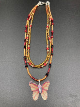 Load image into Gallery viewer, This intricately crafted pendant features a Basil leaf molded in Sterling Silver and adorned with stunningly vivid red, gold, and black glass beaded necklace. Its eye-catching butterfly design adds a bold, yet whimsical touch, making it an ideal choice for a summer look. Necklace is 15 1/2” in length adjustable to 18"