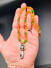 Load image into Gallery viewer, "Amaterasu" Japanese Goddess of the Sun. Necklace is primarily vibrant yellow glass beads that are full of color and shimmer to represent the bright sun. Added a wide range of shimmers of gold and orange and different shades of yellow. Larger green glass beads with small gold beads to really stand out and give the necklace a different dimension and feel. This vibrant goddess necklace is the perfect pop of color to any outfit. Necklace is 16 1/2” adjustable to 19" - pendant is nickel free 1 1/2”