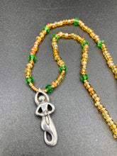 Load image into Gallery viewer, "Amaterasu" Japanese Goddess of the Sun. Necklace is primarily vibrant yellow glass beads that are full of color and shimmer to represent the bright sun. Added a wide range of shimmers of gold and orange and different shades of yellow. Larger green glass beads with small gold beads to really stand out and give the necklace a different dimension and feel. This vibrant goddess necklace is the perfect pop of color to any outfit. Necklace is 16 1/2” adjustable to 19" - pendant is nickel free 1 1/2”