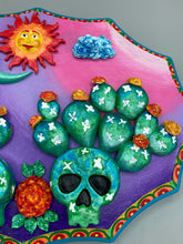 Load image into Gallery viewer, This handcrafted polymer clay wall art features a wood frame painted in a gradient from light pink to dark purple, creating a stunning sunset look. With two bright green skull cactus plant and bright yellow orange blooming flowers. Featuring a vivid sun and crescent moon with a backdrop of dark blue clouds, this frame is sure to make an impression. A bight teal and yellow hue frame to make a bold contrast with the warm background hue. This piece is sure to make a statement.