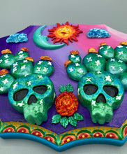 Load image into Gallery viewer, This handcrafted polymer clay wall art features a wood frame painted in a gradient from light pink to dark purple, creating a stunning sunset look. With two bright green skull cactus plant and bright yellow orange blooming flowers. Featuring a vivid sun and crescent moon with a backdrop of dark blue clouds, this frame is sure to make an impression. A bight teal and yellow hue frame to make a bold contrast with the warm background hue. This piece is sure to make a statement.