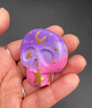 Load image into Gallery viewer, Ideal magnet design to adorn your refrigerator, lockers, workstation, toolbox, or dishwasher. This unique skull statuette features intricate details and vibrant colors, inspired by the summer sky at sundown. Variations in color from purple to light pink simulate the dramatic ombre seen in a setting sun, completed with golden stars and moon silhouettes for a celestial touch. H 1 1/2” x W 1 1/2” x D 3/4”