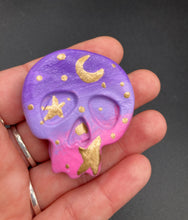 Load image into Gallery viewer, Ideal magnet design to adorn your refrigerator, lockers, workstation, toolbox, or dishwasher. This unique skull statuette features intricate details and vibrant colors, inspired by the summer sky at sundown. Variations in color from purple to light pink simulate the dramatic ombre seen in a setting sun, completed with golden stars and moon silhouettes for a celestial touch. H 1 1/2” x W 1 1/2” x D 3/4”