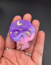 Load image into Gallery viewer, Perfect magnet design to adorn your refrigerator, lockers, workstation, toolbox, or dishwasher. This unique skull statuette features intricate details and vibrant colors, inspired by the summer sky at sundown. Variations in color from purple to light pink simulate the dramatic ombre seen in a setting sun, completed with golden stars and moon silhouettes for a celestial touch.   H 1 1/2” x W 1 1/2” x D 3/4”