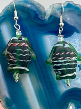 Load image into Gallery viewer, These nature-inspired glass fish earrings are the perfect addition to your boho look. Featuring a delightful dark green hue, the large puffy fish will bring a hippie vibe to your style. Measurements: 1 1/2” in length