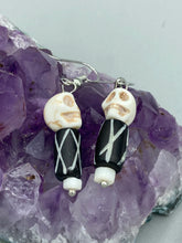 Load image into Gallery viewer, This set of earrings features a mini howlite skull bead with a wood carved black and white bead. Perfect for any goth, emo, witchy, or Day of the Dead outfit, it adds a unique touch to any ensemble. Measurements: 1 1/2 ” in length
