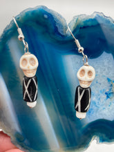 Load image into Gallery viewer, This set of earrings features a mini howlite skull bead with a wood carved black and white bead. Perfect for any goth, emo, witchy, or Day of the Dead outfit, it adds a unique touch to any ensemble. Measurements: 1 1/2 ” in length