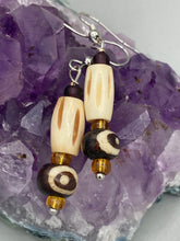 Load image into Gallery viewer, This set of earrings features a cylinder bone bead and round bone bead with eye design and a gold-tone glass bead. Neutral colors allow for versatile styling; the resulting look is sure to be unique.  Measurements: 1 1/2 ” in length
