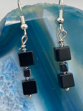 Load image into Gallery viewer, This pair of earrings features two large square-shaped black obsidian beads and small square-shaped hematite beads. With its distinct yet versatile look, this item is sure to make a statement. Measurements: 1” in length