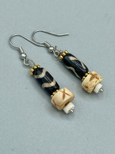 Load image into Gallery viewer, This set of earrings is a one-of-a-kind combination of cylinder and round bone beads with wavy line designs, enhanced with a floral gold tone metal bead set. One earring features vertical wavy lines and crosses, while the other showcases horizontal wavy lines with an "x". The neutral colors make them easy to pair with any ensemble, adding an individualized touch that will make your outfit stand out. Measurements: 1 1/2 ” in length