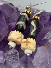 Load image into Gallery viewer, This set of earrings is a one-of-a-kind combination of cylinder and round bone beads with wavy line designs, enhanced with a floral gold tone metal bead set. One earring features vertical wavy lines and crosses, while the other showcases horizontal wavy lines with an "x". The neutral colors make them easy to pair with any ensemble, adding an individualized touch that will make your outfit stand out. Measurements: 1 1/2 ” in length