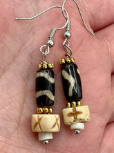 Load image into Gallery viewer, This set of earrings is a one-of-a-kind combination of cylinder and round bone beads with wavy line designs, enhanced with a floral gold tone metal bead set. One earring features vertical wavy lines and crosses, while the other showcases horizontal wavy lines with an "x". The neutral colors make them easy to pair with any ensemble, adding an individualized touch that will make your outfit stand out. Measurements: 1 1/2 ” in length