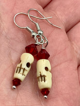 Load image into Gallery viewer, These handcrafted earrings feature a mini-bone carved skull coupled with dark red glass beads. Perfect for Goth, Emo, and Witchy styles, these earrings are sure to provide a unique addition to any Day of the Dead outfit. Our earrings can effortlessly transition between dressy and casual styles. Measurements: 1 1/4 ” in length