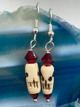 Load image into Gallery viewer, These handcrafted earrings feature a mini-bone carved skull coupled with dark red glass beads. Perfect for Goth, Emo, and Witchy styles, these earrings are sure to provide a unique addition to any Day of the Dead outfit. Our earrings can effortlessly transition between dressy and casual styles. Measurements: 1 1/4 ” in length