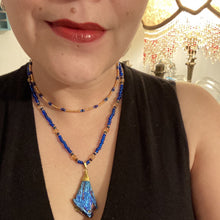 Load image into Gallery viewer, A bold deep blue kyanite wired stone pendant is surrounded by two strands of glass bead necklaces featuring a deep blue and gold shimmer palette. The shorter strand is designed to be worn as a collar or choker, while the longer second strand creates a striking contrast. With its bold appearance and eye-catching gemstone pendant, this necklace is a must-have for any jewelry collection. Necklace is 15” in length, can be adjusted to 18"