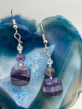Load image into Gallery viewer, This luxurious set of earrings feature large square-shaped rainbow fluorite beads contrasted against round amethyst beads, presenting an elegant neutral yet cool-toned look. With its unique and versatile style, these earrings make a perfect addition to any wardrobe. Measurements: 1 3/8” in length
