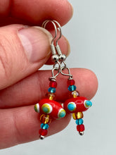 Load image into Gallery viewer, This eye-catching set of earrings features colorful, bumpy round lampworked glass beads in vivid shades of fire engine red, white, green, and orange. An iconic fiesta piñata-shaped bead completes the unique and bold design, but also reminiscent of a virus. A spectacular accessory, these earrings are sure to draw attention.  Measurements: 1 1/4” in length