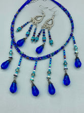 Load image into Gallery viewer, This set of large, eye-catching chandelier-style earrings draw inspiration from the vibrant array of colors found in the galaxy and cosmos. Featuring three strands of shimmering glass beads in bold shades of blue, purple, gold, and green, it's an essential piece for any jewelry collection. Measurements: 3 1/2” in length