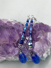 Load image into Gallery viewer, This stunning, one of a kind pair of celestial beaded earrings is a bold addition to any jewelry collection. Crafted with vibrant blue glass beads, the color contains varied shades of blue, purple, and hints of gold to create unique texture. The design is inspired by the awe-inspiring beauty of the majestic galaxy. Measurements: 2 3/4” in length