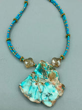 Load image into Gallery viewer, This vibrant and striking double strand necklace features a combination of glass beads in blue and green shades of turquoise, gold and champagne. The two delicate strands are accented with a gold-tone flower-shaped bead, a howlite stone chip dyed in turquoise, and shimmery, cross-faceted champagne-colored glass beads to complete the dramatic look. Measurements: Necklace is 17” and can be adjusted up to 19"