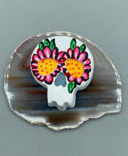 Load image into Gallery viewer, Heal emotionally and spiritually through art by honoring a loved one with a unique and beautiful Purple Spirit Piece Memorial Skull Art. Day Of The Dead Spirit Piece is an ideal addition to your ofrenda or altar that will provide a lasting tribute. These handcrafted polymer clay skull figurines are adorned with hand-painted pink floral designs for the eyes. H 1 1/2” x W 1 1/2” x D 3/4”
