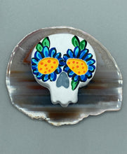 Load image into Gallery viewer, Heal emotionally and spiritually through art by honoring a loved one with a unique and beautiful Purple Spirit Piece Memorial Skull Art. Day Of The Dead Spirit Piece is an ideal addition to your ofrenda or altar that will provide a lasting tribute. These handcrafted polymer clay skull figurines are adorned with hand-painted dark blue floral designs for the eyes. H 1 1/2” x W 1 1/2” x D 3/4”