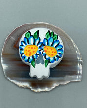 Load image into Gallery viewer, Heal emotionally and spiritually through art by honoring a loved one with a unique and beautiful Purple Spirit Piece Memorial Skull Art. Day Of The Dead Spirit Piece is an ideal addition to your ofrenda or altar that will provide a lasting tribute. These handcrafted polymer clay skull figurines are adorned with hand-painted light blue floral designs for the eyes. H 1 1/2” x W 1 1/2” x D 3/4”