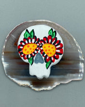 Load image into Gallery viewer, Heal emotionally and spiritually through art by honoring a loved one with a unique and beautiful Purple Spirit Piece Memorial Skull Art. Day Of The Dead Spirit Piece is an ideal addition to your ofrenda or altar that will provide a lasting tribute. These handcrafted polymer clay skull figurines are adorned with hand-painted red floral designs for the eyes. H 1 1/2” x W 1 1/2” x D 3/4”