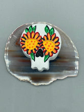 Load image into Gallery viewer, Heal emotionally and spiritually through art by honoring a loved one with a unique and beautiful Purple Spirit Piece Memorial Skull Art. Day Of The Dead Spirit Piece is an ideal addition to your ofrenda or altar that will provide a lasting tribute. These handcrafted polymer clay skull figurines are adorned with hand-painted bright orange floral designs for the eyes. H 1 1/2” x W 1 1/2” x D 3/4”