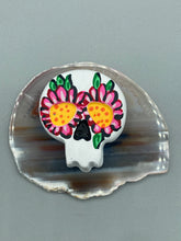 Load image into Gallery viewer, Heal emotionally and spiritually through art by honoring a loved one with a unique and beautiful Purple Spirit Piece Memorial Skull Art. Day Of The Dead Spirit Piece is an ideal addition to your ofrenda or altar that will provide a lasting tribute. These handcrafted polymer clay skull figurines are adorned with hand-painted pink floral designs for the eyes. H 1 1/2” x W 1 1/2” x D 3/4”
