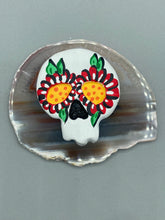 Load image into Gallery viewer, Heal emotionally and spiritually through art by honoring a loved one with a unique and beautiful Purple Spirit Piece Memorial Skull Art. Day Of The Dead Spirit Piece is an ideal addition to your ofrenda or altar that will provide a lasting tribute. These handcrafted polymer clay skull figurines are adorned with hand-painted red floral designs for the eyes. H 1 1/2” x W 1 1/2” x D 3/4”