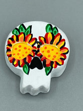 Load image into Gallery viewer, Heal emotionally and spiritually through art by honoring a loved one with a unique and beautiful Purple Spirit Piece Memorial Skull Art. Day Of The Dead Spirit Piece is an ideal addition to your ofrenda or altar that will provide a lasting tribute. These handcrafted polymer clay skull figurines are adorned with hand-painted bright yellow floral designs for the eyes. H 1 1/2” x W 1 1/2” x D 3/4”