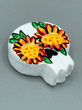 Load image into Gallery viewer, Heal emotionally and spiritually through art by honoring a loved one with a unique and beautiful Purple Spirit Piece Memorial Skull Art. Day Of The Dead Spirit Piece is an ideal addition to your ofrenda or altar that will provide a lasting tribute. These handcrafted polymer clay skull figurines are adorned with hand-painted bright yellow floral designs for the eyes. H 1 1/2” x W 1 1/2” x D 3/4”