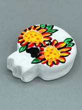 Load image into Gallery viewer, Heal emotionally and spiritually through art by honoring a loved one with a unique and beautiful Purple Spirit Piece Memorial Skull Art. Day Of The Dead Spirit Piece is an ideal addition to your ofrenda or altar that will provide a lasting tribute. These handcrafted polymer clay skull figurines are adorned with hand-painted bright yellow floral designs for the eyes. H 1 1/2” x W 1 1/2” x D 3/4”